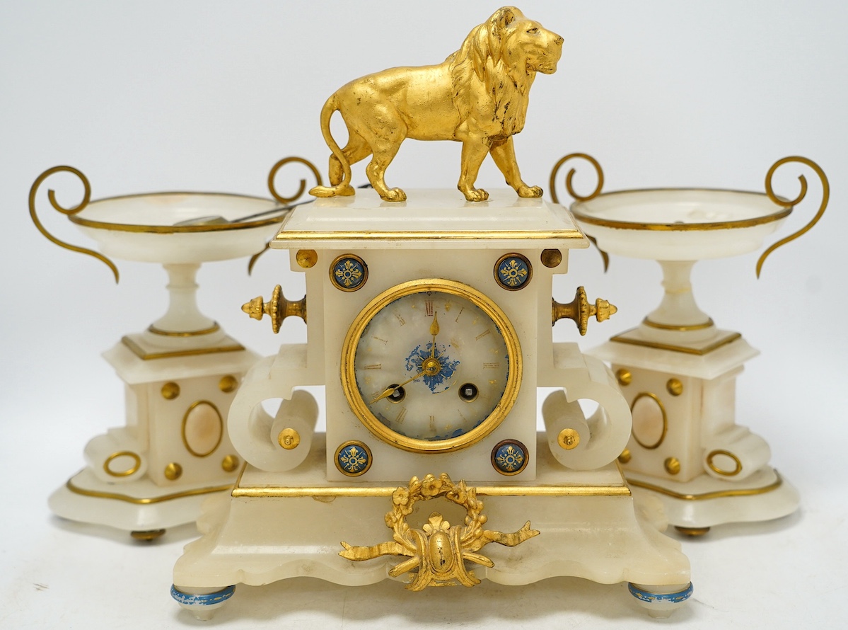An early 20th century alabaster and gilt metal clock garniture with enamel panels, surmounted with a lion, with pendulum, no key, clock 30cm high. Condition - poor